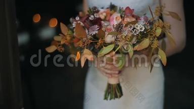 新娘手中的婚礼花束在室内。 在背景上点燃蜡烛。 新娘手里捧着漂亮的婚礼花束